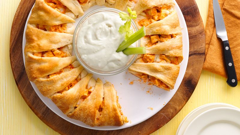 Buffalo Chicken Crescent Ring prepared recipe on a tray with a bowl of dipping sauce in the middle of the ring